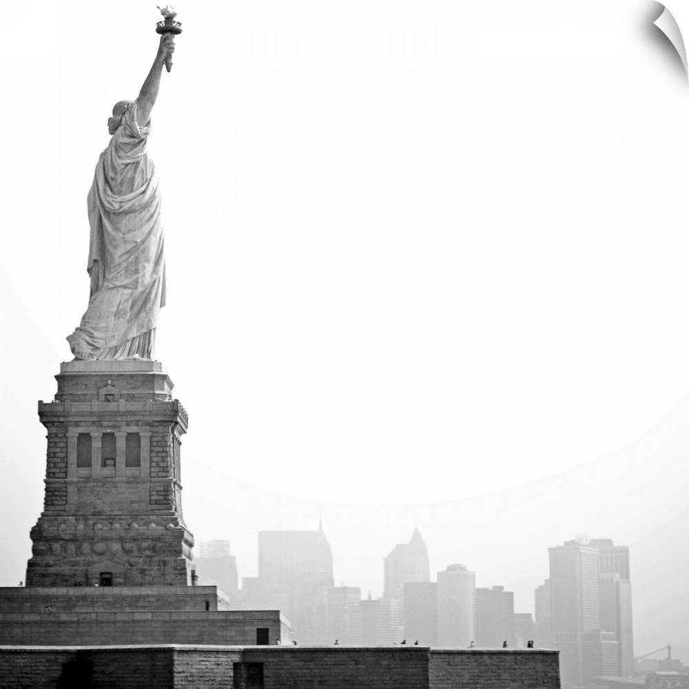 Black and white image of statue of Liberty with island of Manhattan/New York City in background.