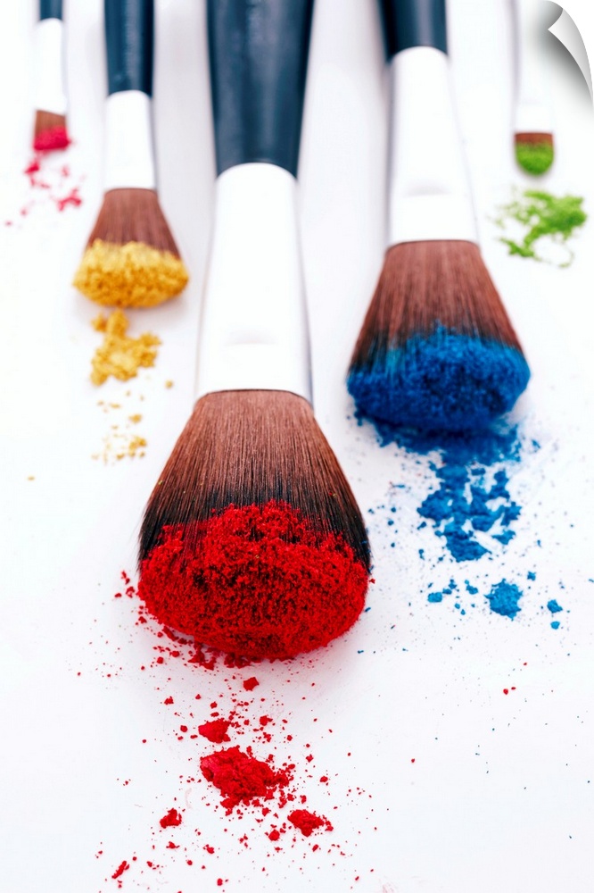 A vertical photo of makeup brushes heavily filled with pigment resting on blank a surface.