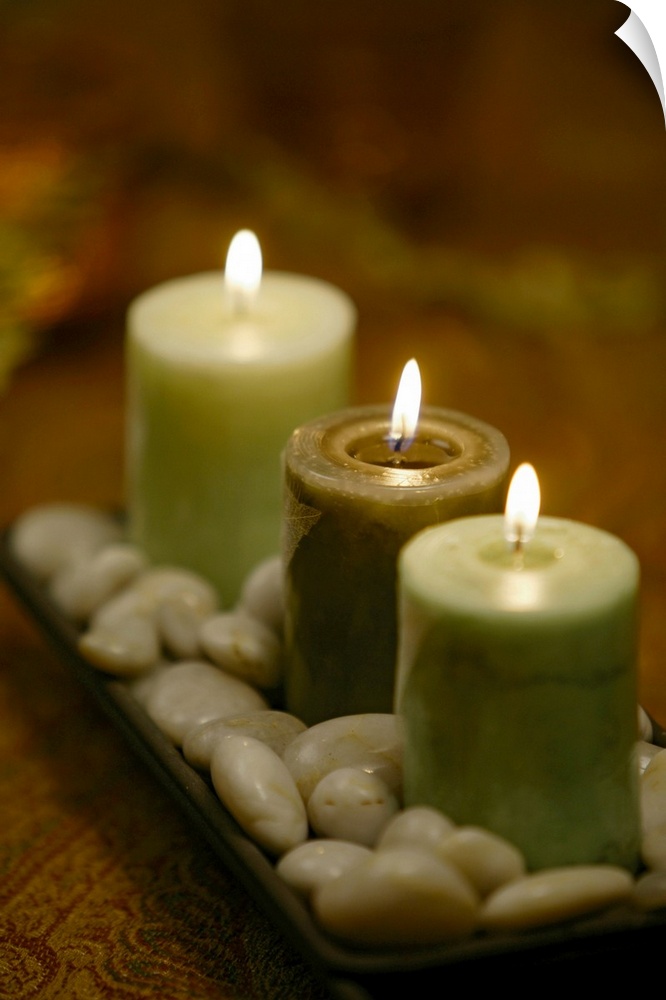 Relaxing photograph of three lit candles resting in a shallow dish of round, polished pebbles.