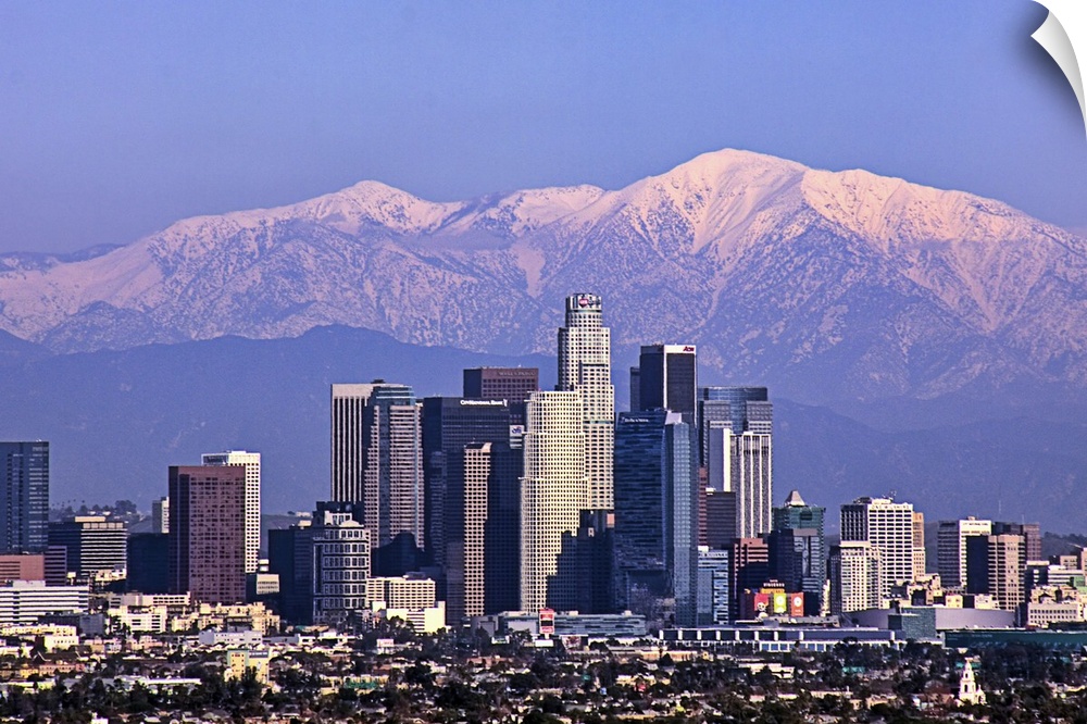 This large piece is a photograph large buildings in Los Angeles with big snow covered mountains in the backdrop.