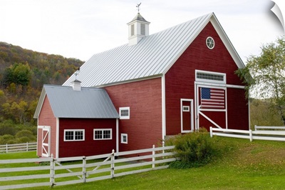 Classic New England farm with red barn and white fence, American flag on barn door