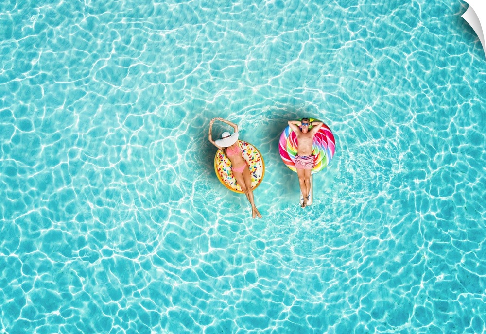 A happy vacation couple in swimsuits enjoys the tropical sun of the Maldives on colorful floats over turquoise colored sea.