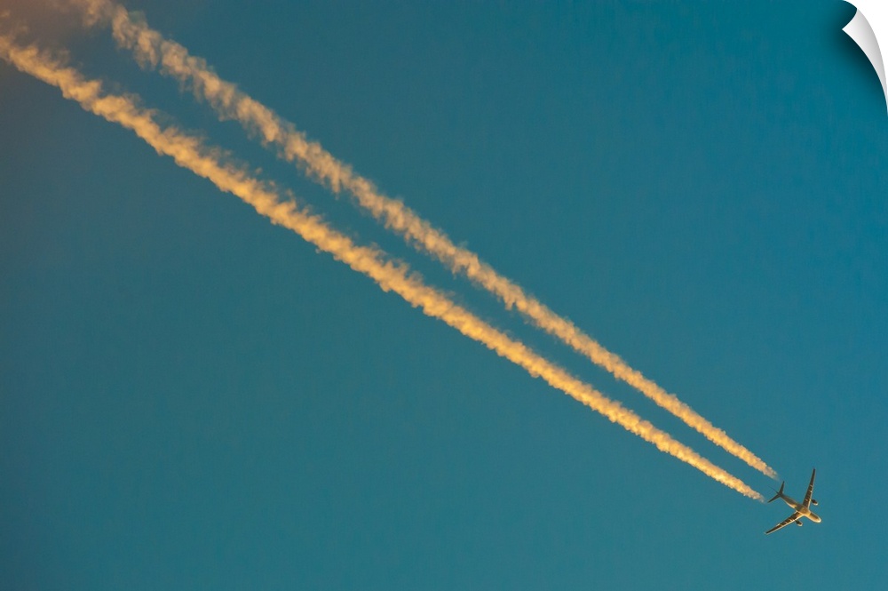 Long condensation trails in blue sky at sunset.