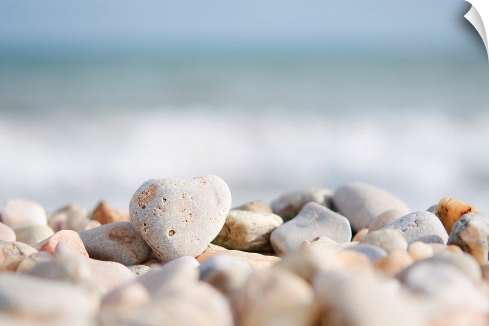 Closeup photograph of a pile of stones on a beach in the foreground. The Mediterranean sea with waves and the sky over the...