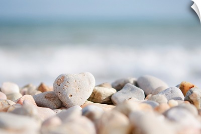 Directed focus on a heart shaped stone on a pebble beach in the foreground.