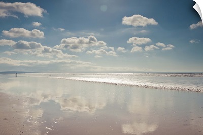 Empty beach with a thin film of water reflecting fluffy clouds in a sunny blue sky.