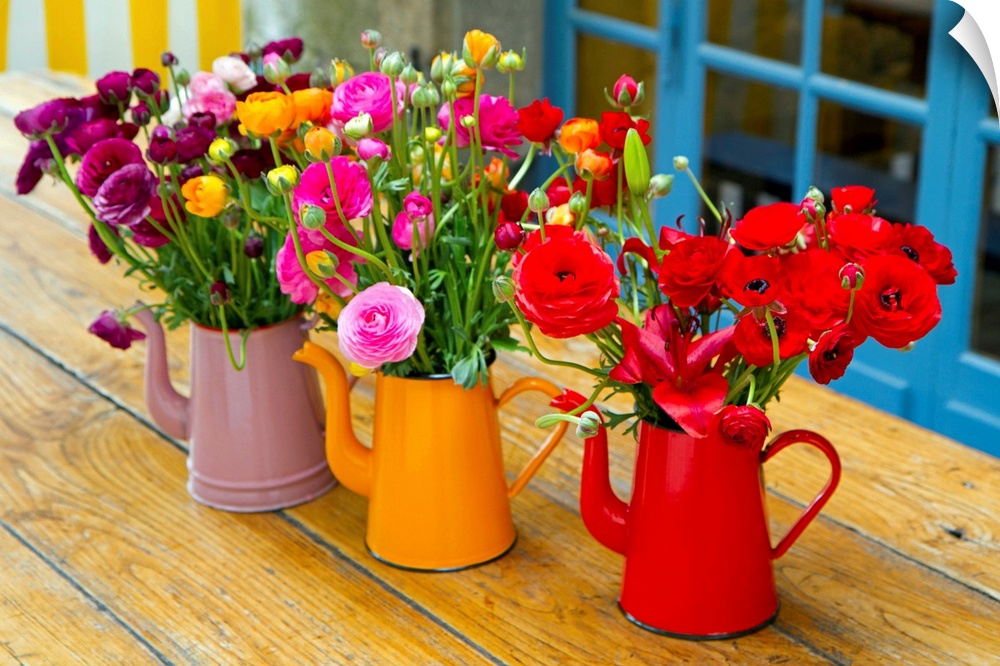 Photograph of three flowerpots sitting on a table with flowers in them.