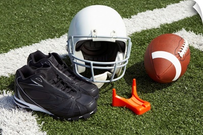 Football, football helmet, tee and shoes on football field