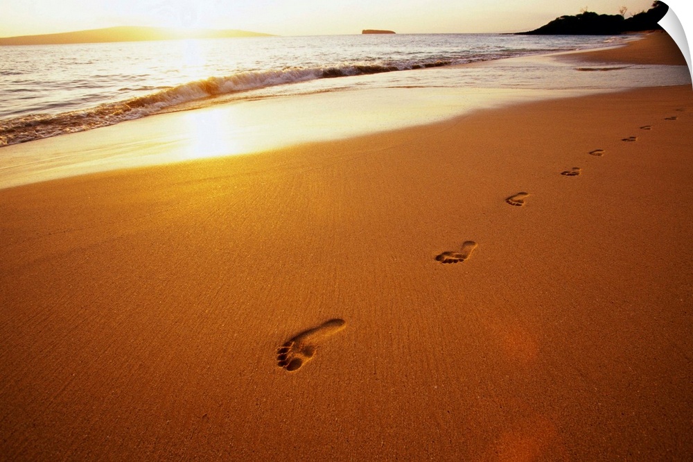 Footprints along Makena Beach on Maui. The setting sun reflects off the sand and surf.