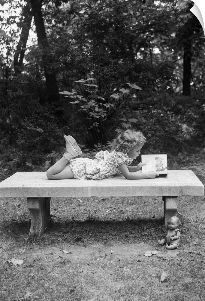 A young girl lies on a bench reading, with her doll on the ground next to her. The scene is framed by grass and trees. Und...