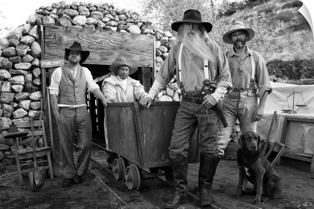 Four men, gold miners and cowboys in front of a mine shaft with a dog