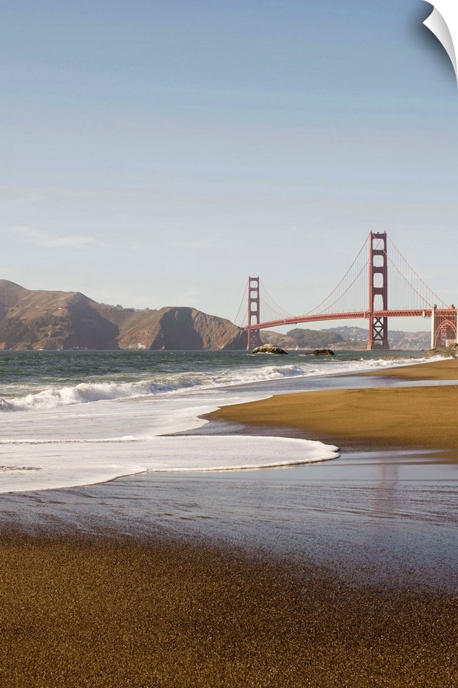 Vertical photograph taken from a distance of the Golden Gate Bridge which a strip of beach and the ocean pictured in the f...