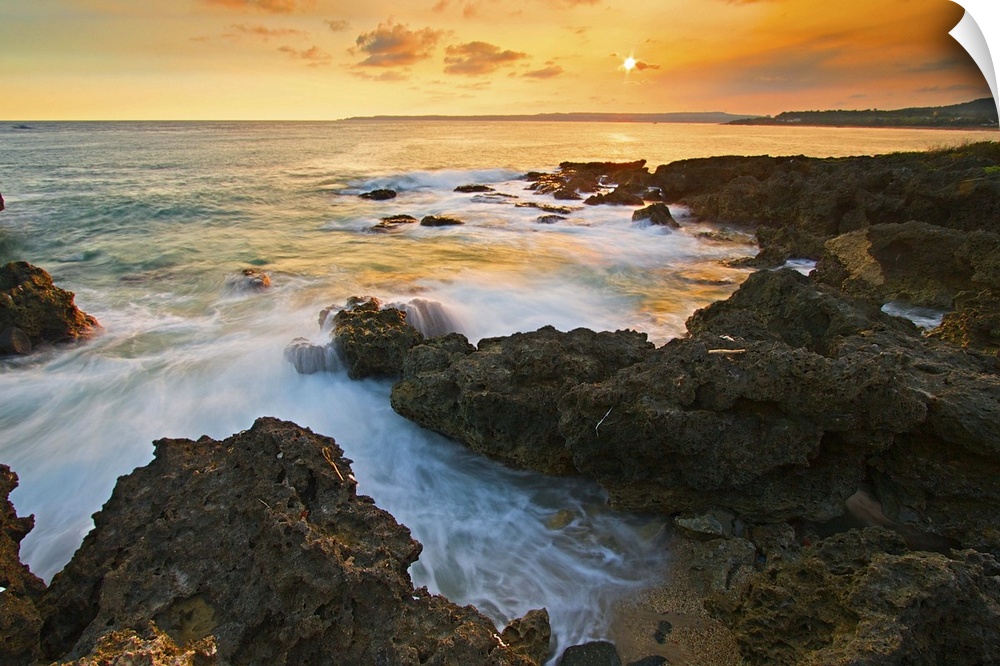 Frog rock in Kenting at golden dusk with foaming waves rushing in and crashing on dark coral reefs while setting sun paint...