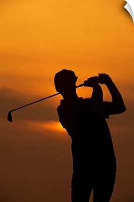 Golfer silhouetted by sunset