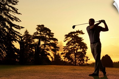 Golfer swinging club on golf course at sunset