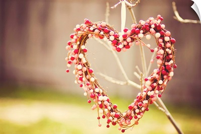 Heart wreath made out of red, white and pink beads hanging on tree.