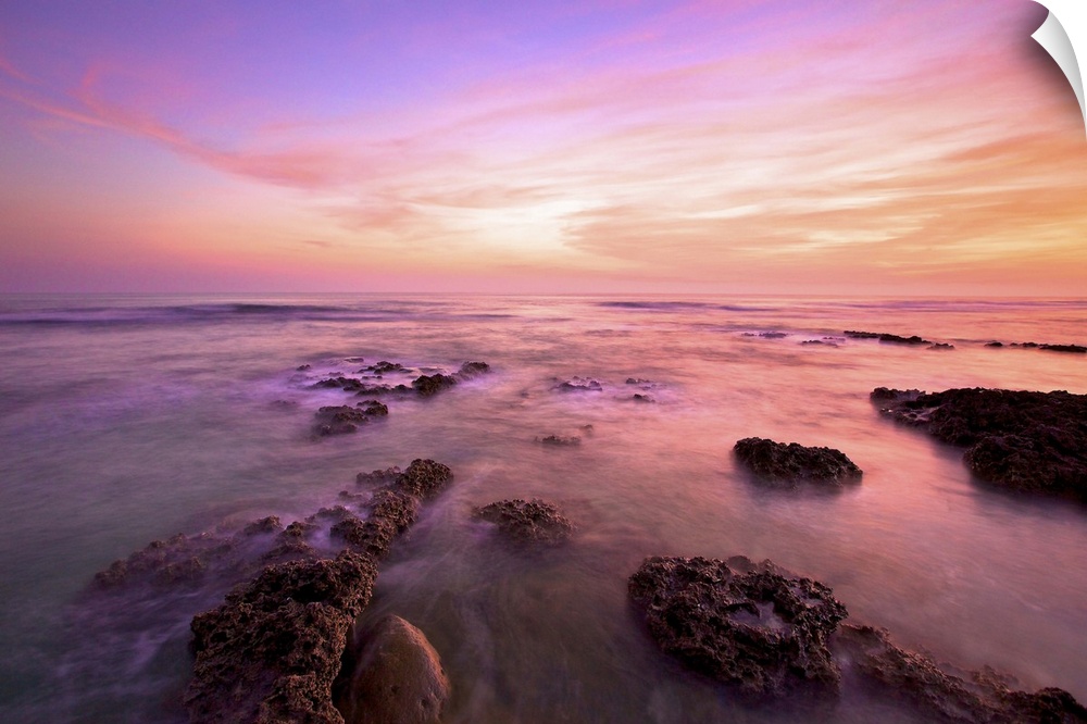 Purple clouds spreading above Wanliton sky at dusk and sea water crashing on coral reefs; in Pingtung, Taiwan.