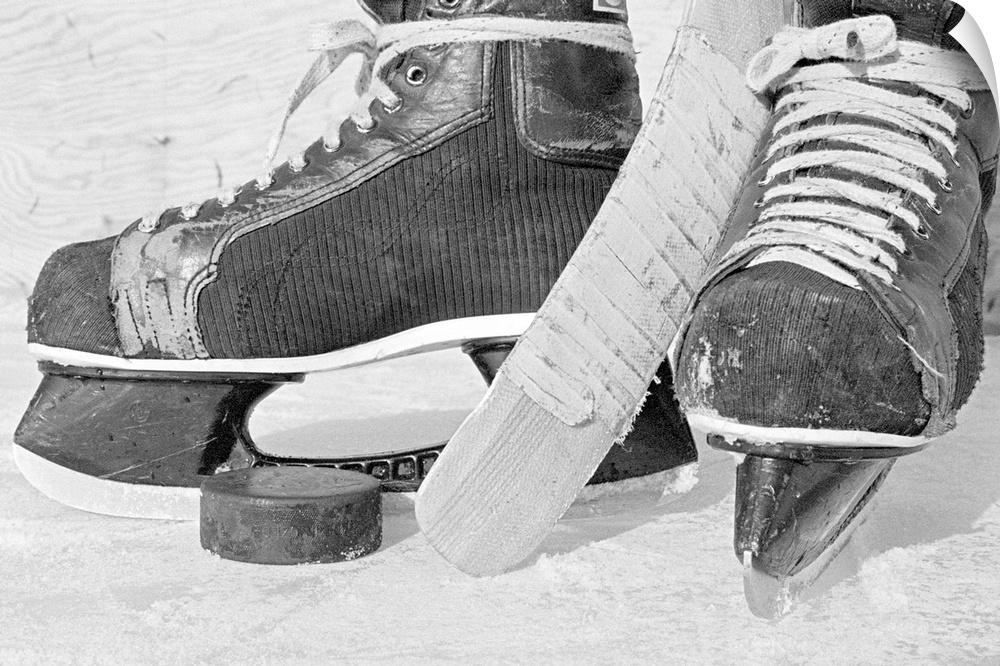 Large, landscape photograph of vintage hockey skates on the ice.  Between the skates is the end of a stick and a hockey puck.