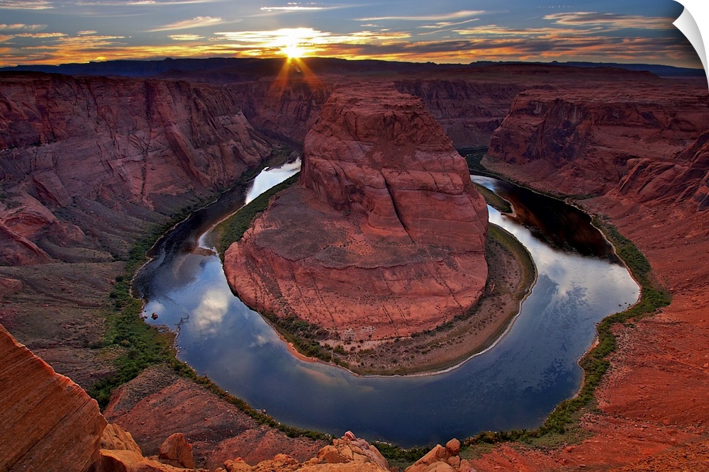 Photograph of river circling huge rock formation at sunset under a cloudy sky.