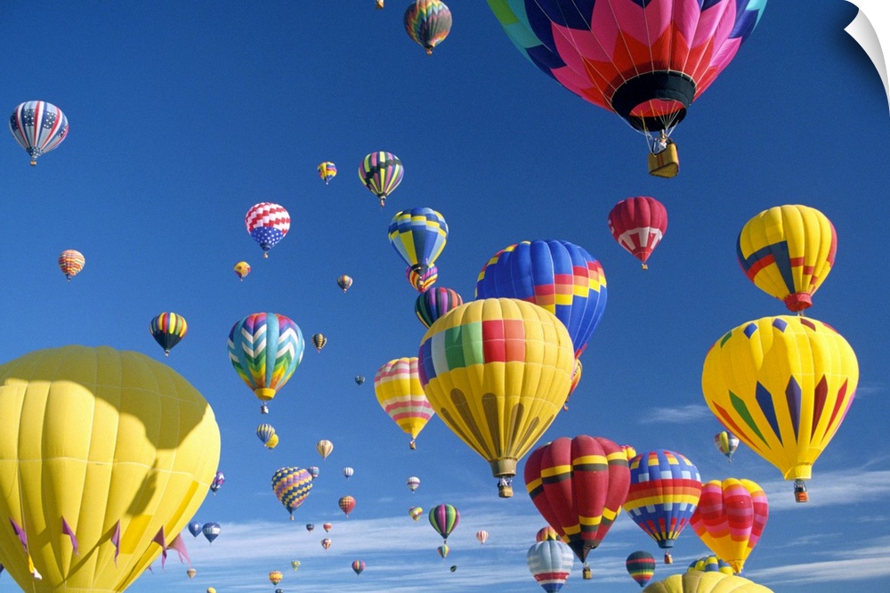 Big, horizontal photograph of many brightly colored hot air balloons with varying patterns, floating against a blue sky.