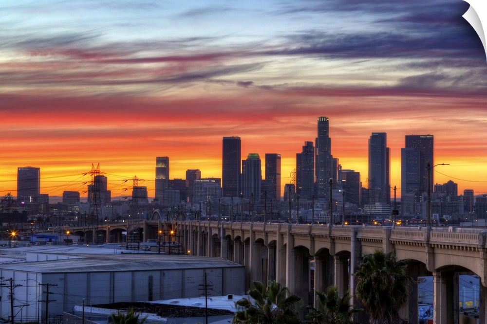 Sunset creates a stunning display on the cloudy sky over a California cityscape with skyscrapers and a bridge.