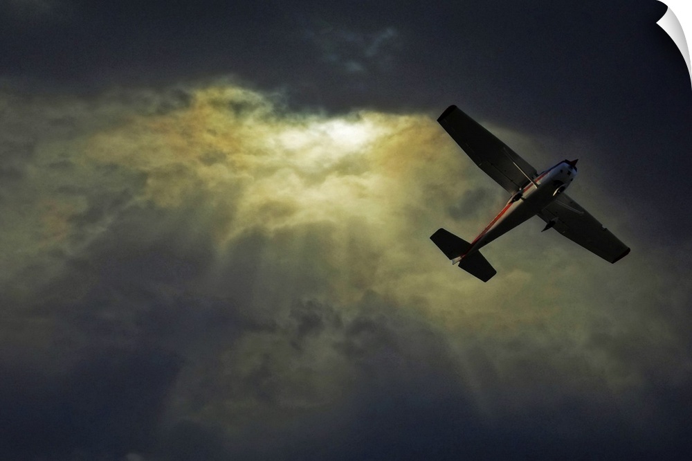 A photograph taken looking upward where rays of sunlight shine through dense cloud cover and a small airplane flies overhead.
