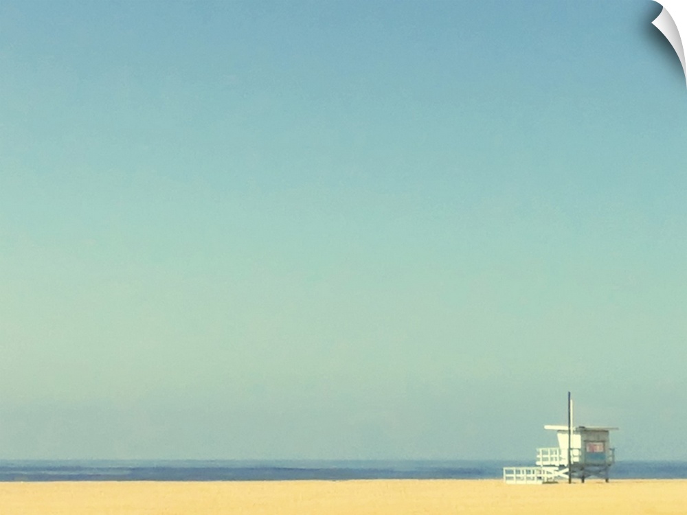 Landscape, oversized photograph of a single lifeguard tower on an empty beach of golden sand, beneath a huge, clear blue sky.