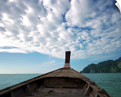 Long boat in sea with cloudy sky and mountain in background.