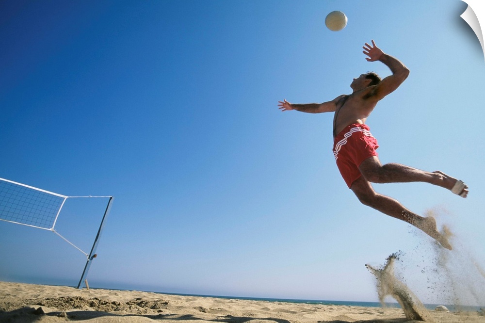 Male beach volleyball player jumping up to spike ball. California, USA.