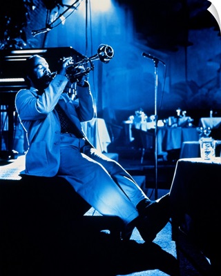 Man sitting on edge of stage, playing trumpet