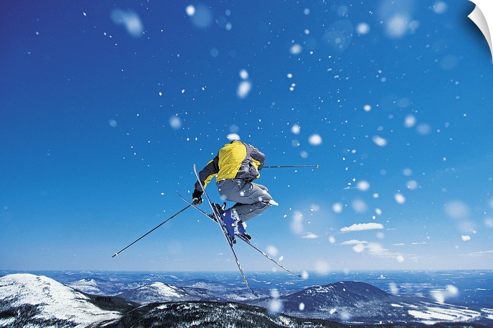 Photograph of man on skis in mid air jump over snow covered mountains.