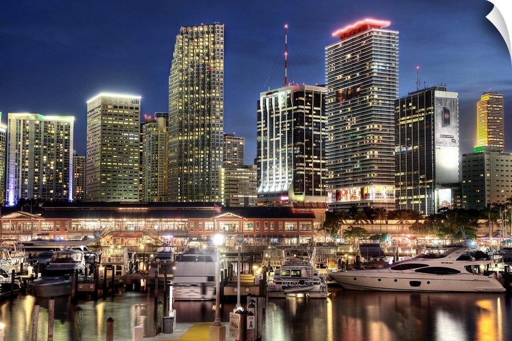 Photograph of the nighttime lit up Miami skyline down at the harbor with boats parked in their water slips.