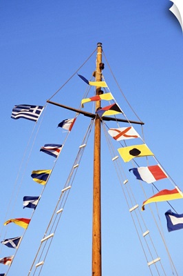 Multiple flags on the mast of a sailboat against a blue sky