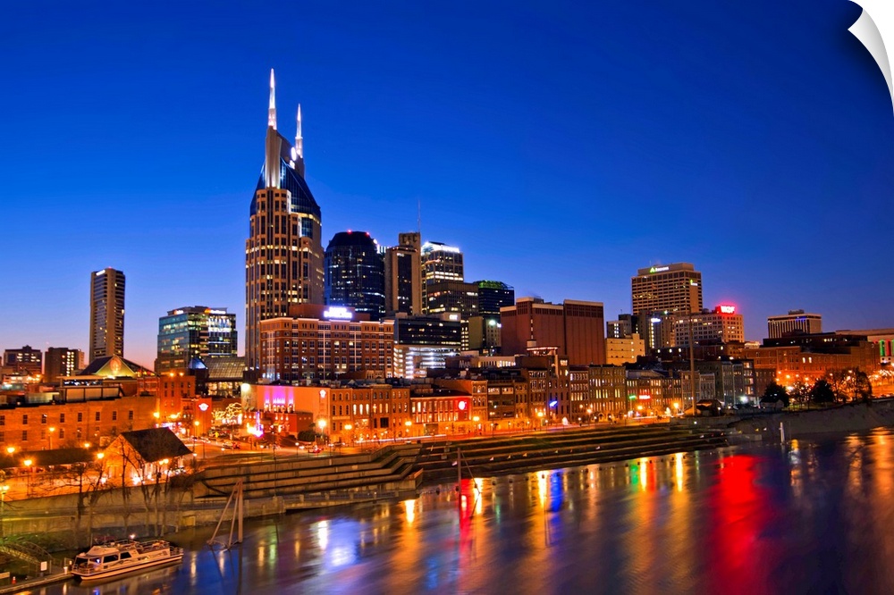 Big, horizontal photograph of the Nashville Tennessee skyline, lit up during blue hour, just after sunset, reflecting in t...