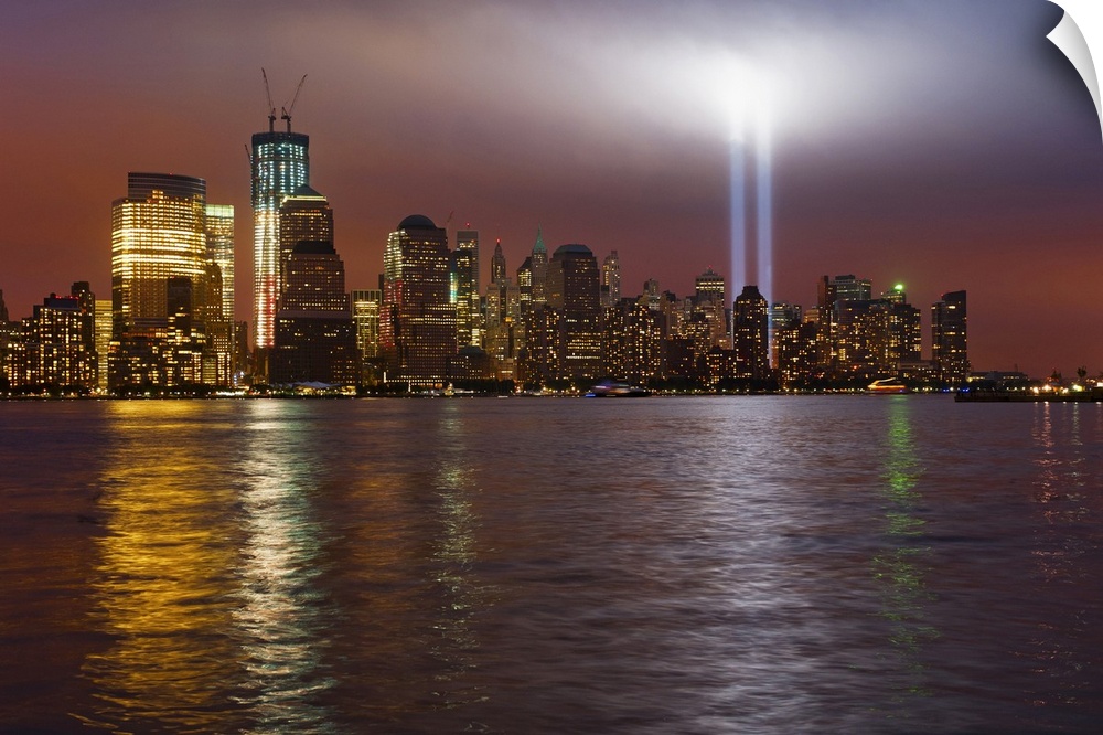 Large, horizontal photograph of New York City, the Manhattan skyline at night, with 9/11 memorial lights.