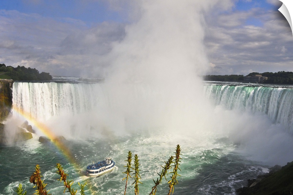 Wide landscape view of waterfall Rainbow in foreground Turquoise color of water Blue sky and white clouds.