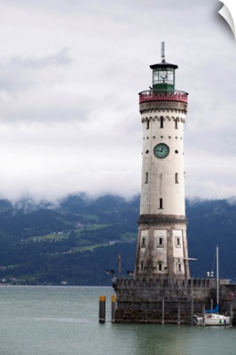 old lighthouse on a pier of a lake with cloud covered mountains in the background