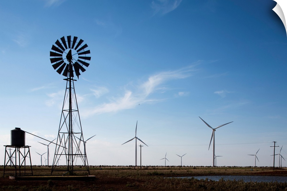 USA, Texas, Vega, Old ranch windmill and water pump beneath array of wind power generating turbines at Wildorado Wind Farm...