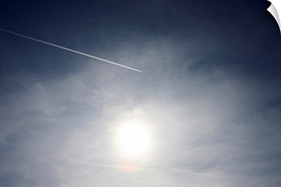 Plane and Vapor trail flying above sun.