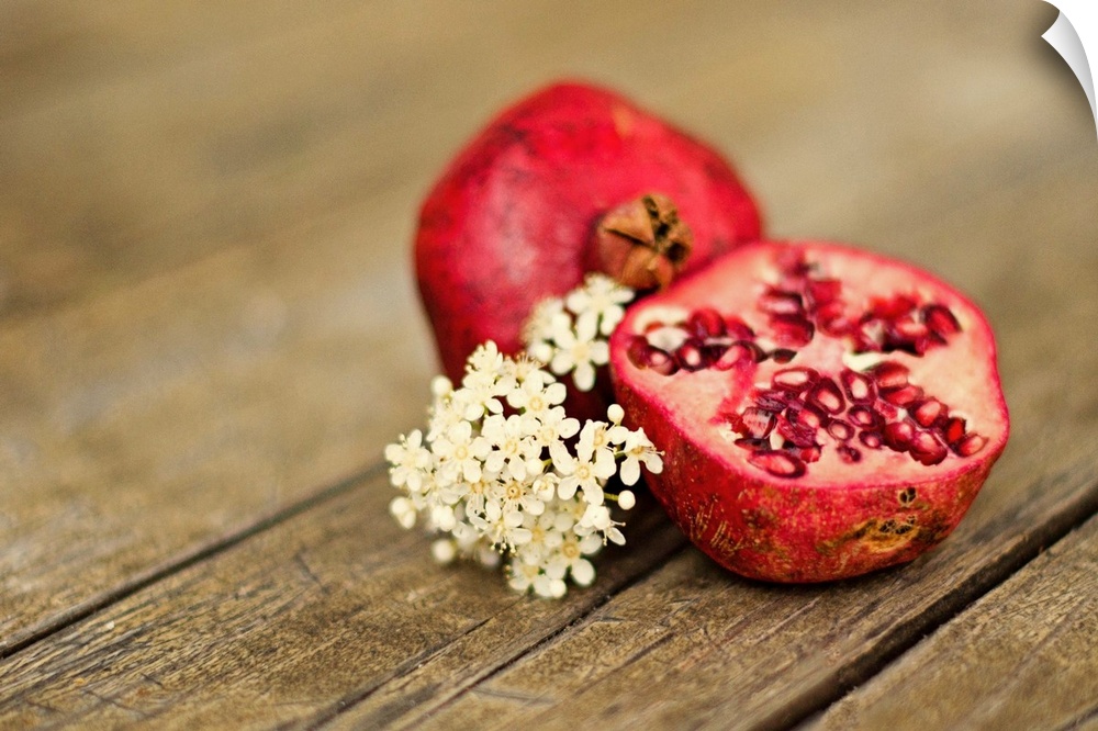 Pomegranate fruit cut in half, with cluster of tiny white flowers on rustic looking wooden tabletop.