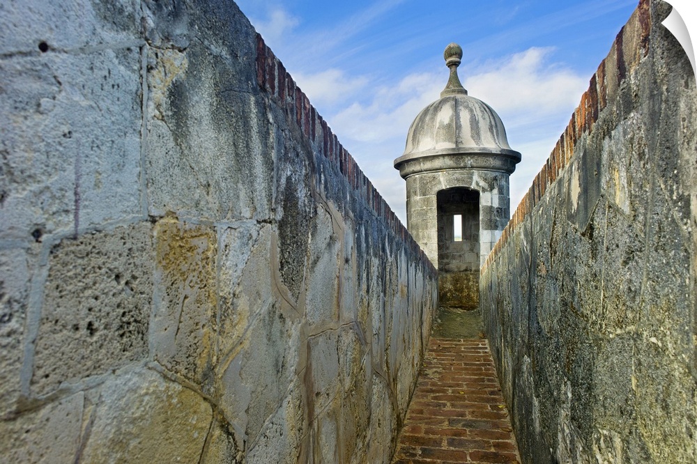 Photograph of pathway lined with tall stone walls leading to a castle's turret.