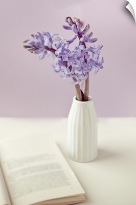 Purple flower vase with open book on table.