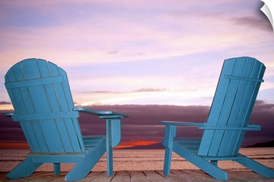 Rear view still life of two blue Adirondack chairs on a boardwalk at the coast.
