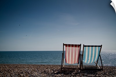 Red and blue striped deckchair facing out to blue sea. Pebble beach and clear blue sky.