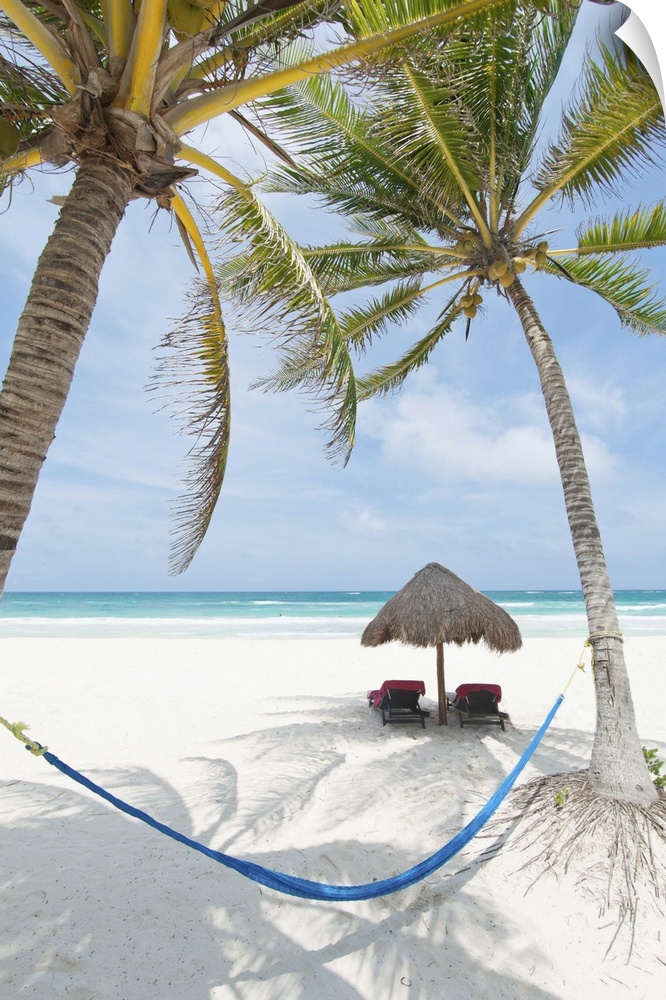 Tropical summer beach resort with chaise lounge beach chairs, hammock and palm trees in Tulum, Mexico.
