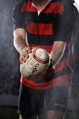 Rugby player holding ball in rain, mid section