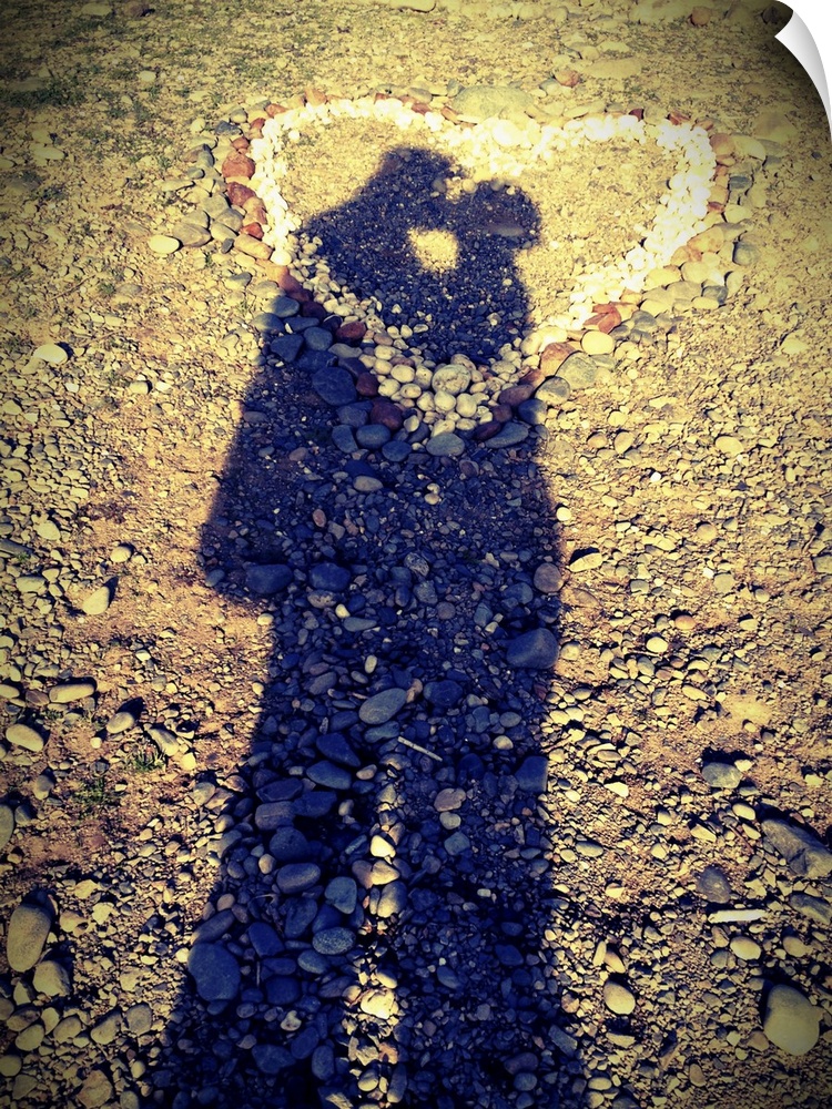Shadows of couple kissing over heart of stones.