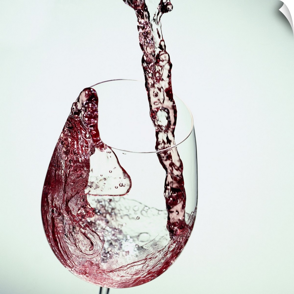 Photograph taken of red wine while being poured into a clear wine glass.