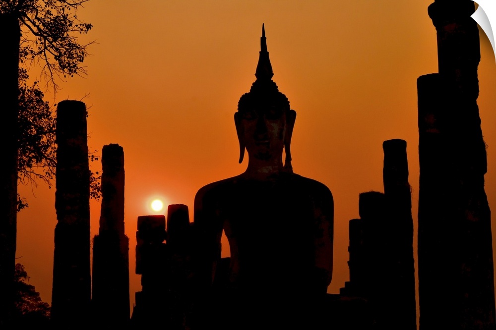 Silhouette of ancient Buddha statue sitting in middle of ruined temple (illustrated by remaining columns) in Sukhothai His...