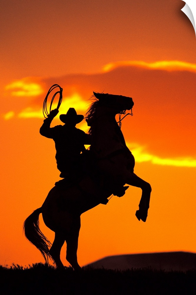 Large artwork of the silhouette of a cowboy on a horse that is standing on it's back two legs in front of a sunset sky.